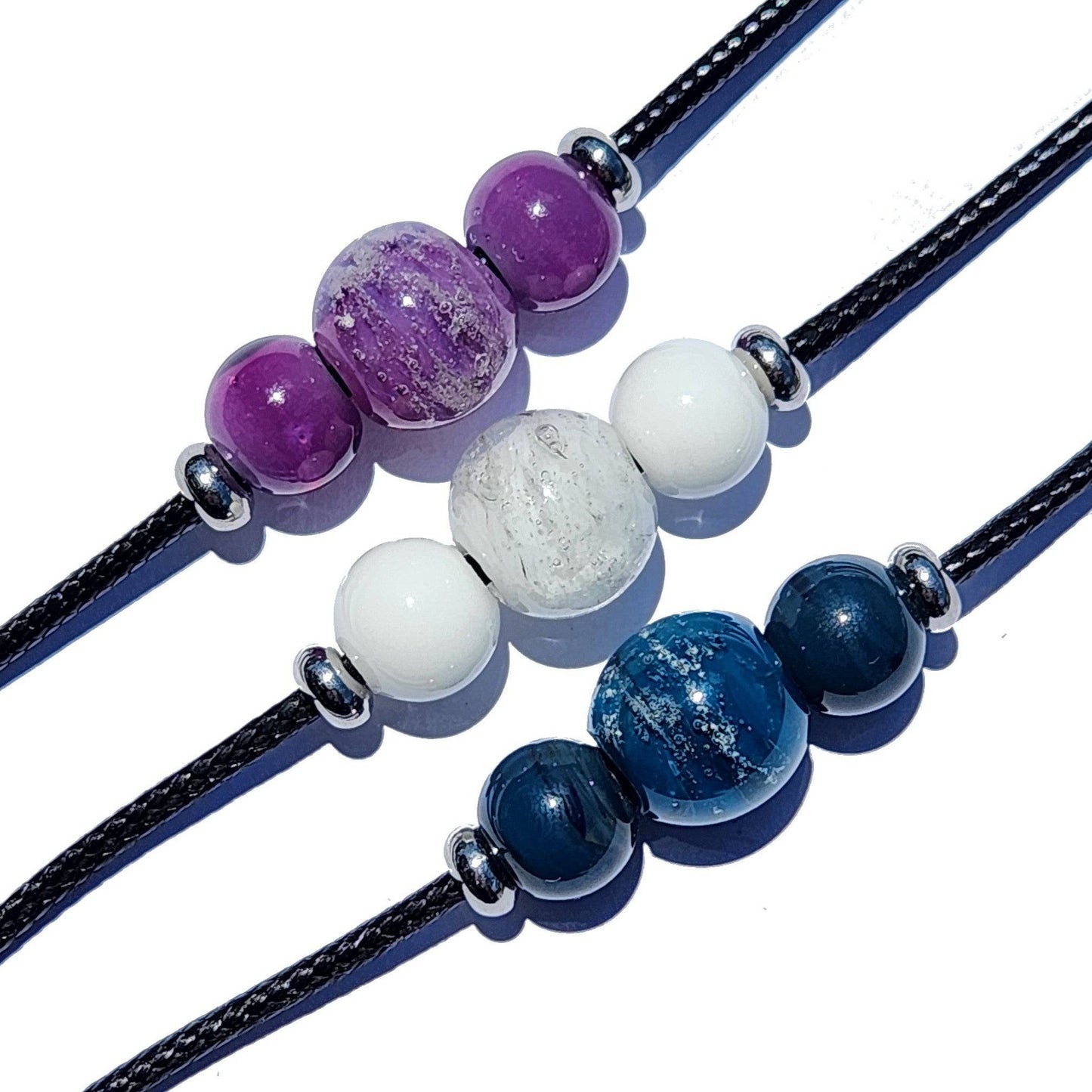 Trio of Forever Close Ashes Necklaces in purple, white, and blue. Ash-infused glass beads on black cord for personalized remembrance.