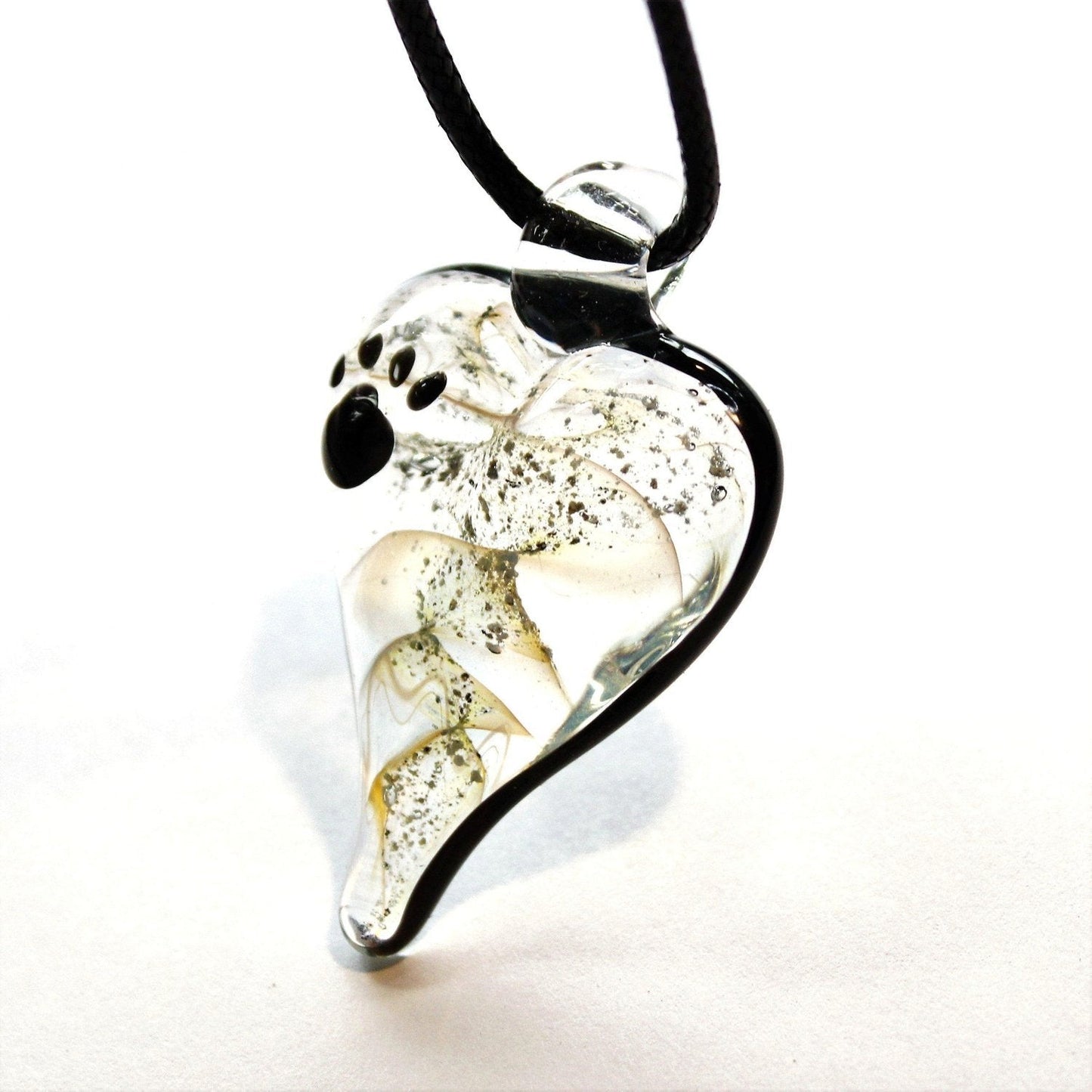 Paw Print Urn Necklace – Heart Pendant for Ashes in clear glass with black paw print and suspended ashes, worn on a black cord necklace.
