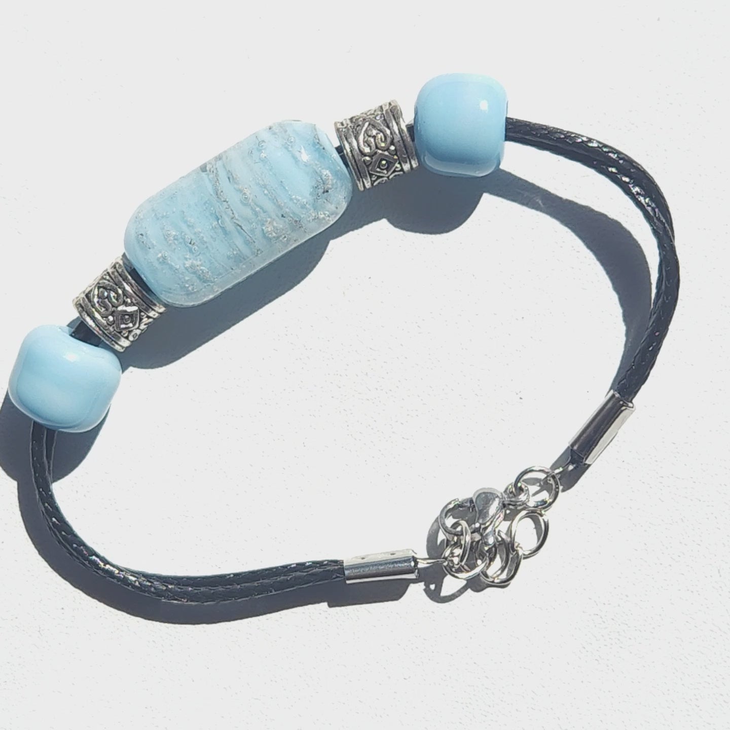 Bracelet with ashes featuring a handmade blue cremation bead, silver heart-accented spacers, and black leather cord. Memorial urn jewelry for daily wear.