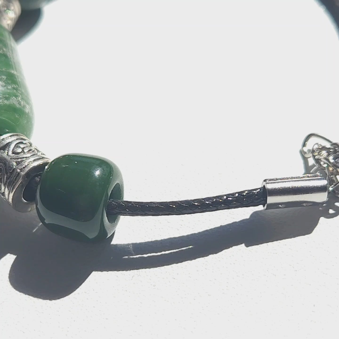 Close-up of Remember Me cremation bracelet with ashes, featuring green cremation bead and stainless steel clasp on black cord. Memorial jewelry for daily wear.