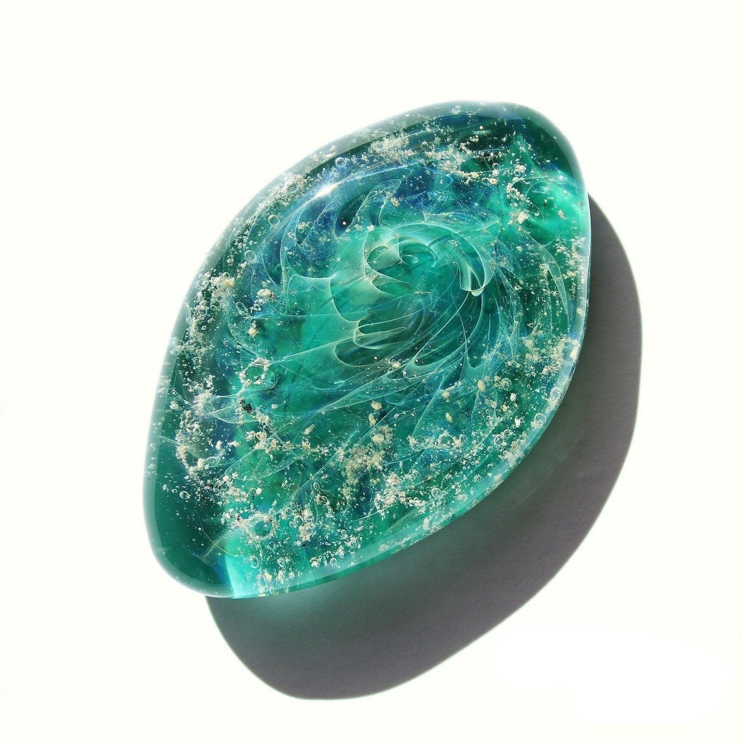 Galaxy Cremation Touchstone in turquoise and teal hues with ashes suspended in glass. Memorial glass keepsake for honoring loved ones.