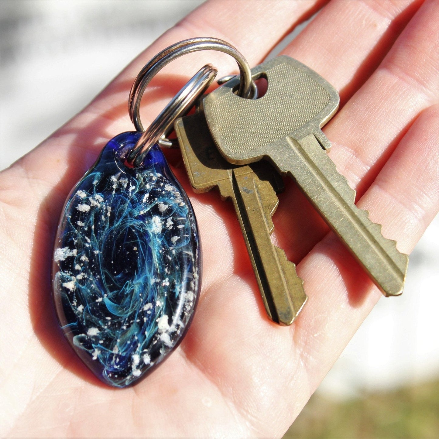 Galaxy Cremation Touchstone keychain with ashes in blue and purple glass, shown in hand with keys for scale. Memorial glass keepsake for remembrance.