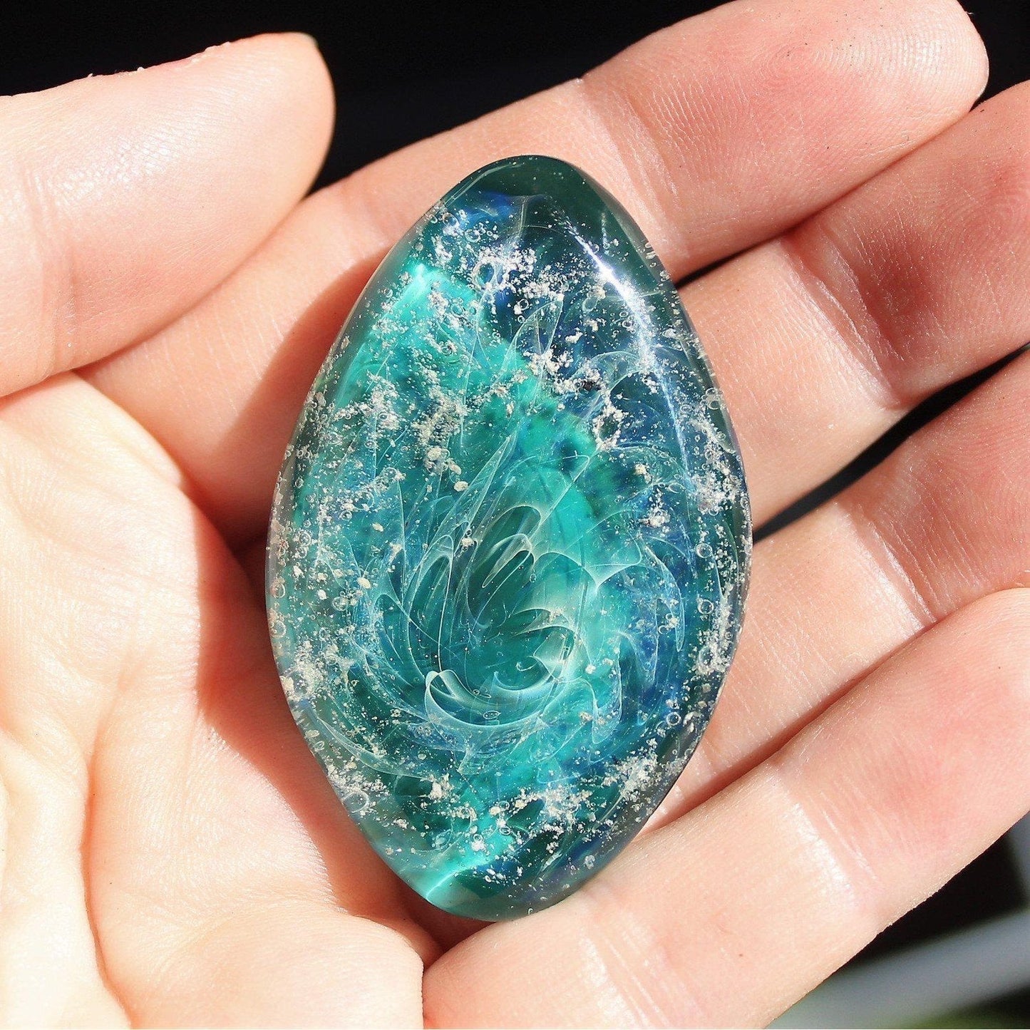 Galaxy Cremation Touchstone | Memorial Glass Keepsake with Ashes in turquoise and blue hues, held in hand. Handmade, durable, and waterproof.