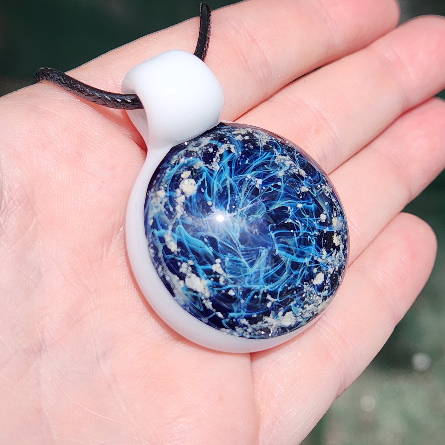 Galaxy Cremation Pendant – Handmade Ashes Memorial Necklace featuring a deep blue glass design with swirling patterns and embedded ashes, set in a white base.