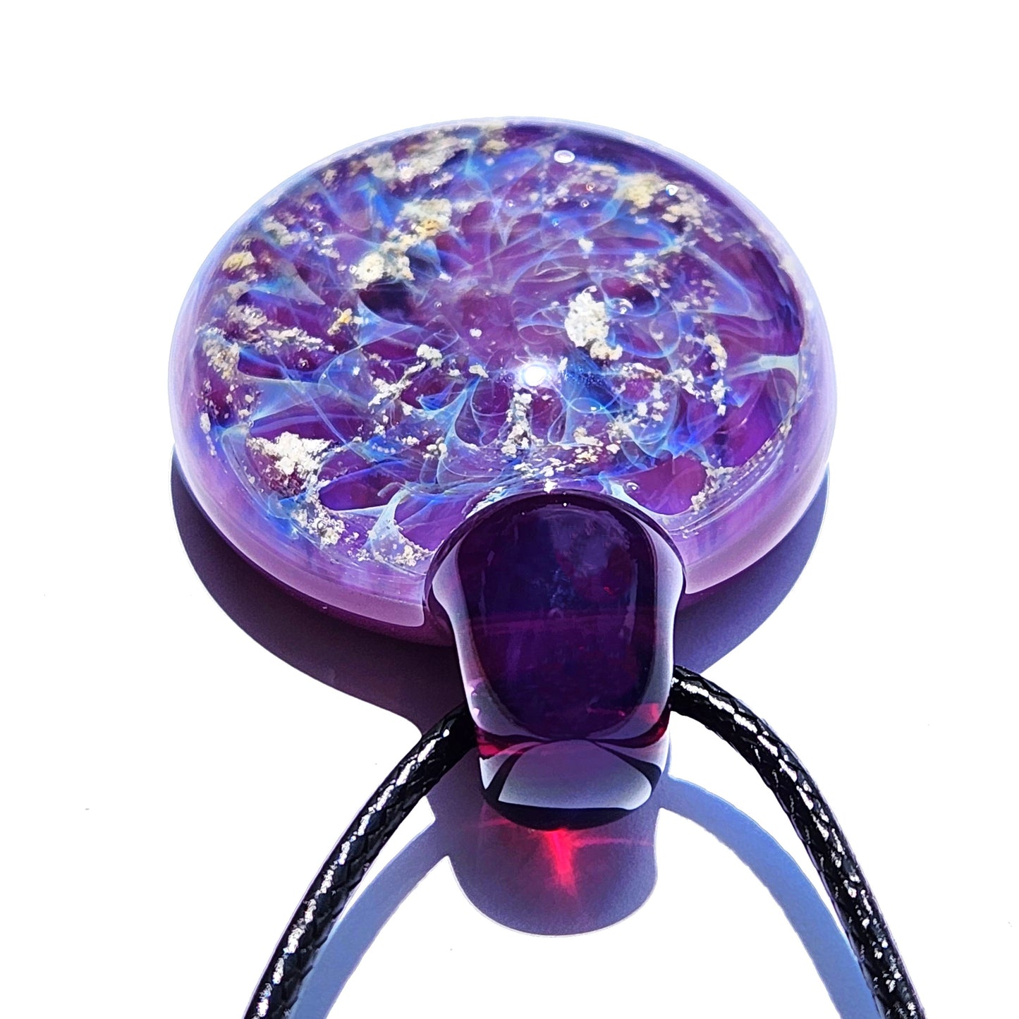 A round, purple glass ashes pendant with a dark purple top. The pendant features a swirling design of light blue and ashes flecks within the glass. The memorial pendant hangs from a black cord, creating a unique necklace.
