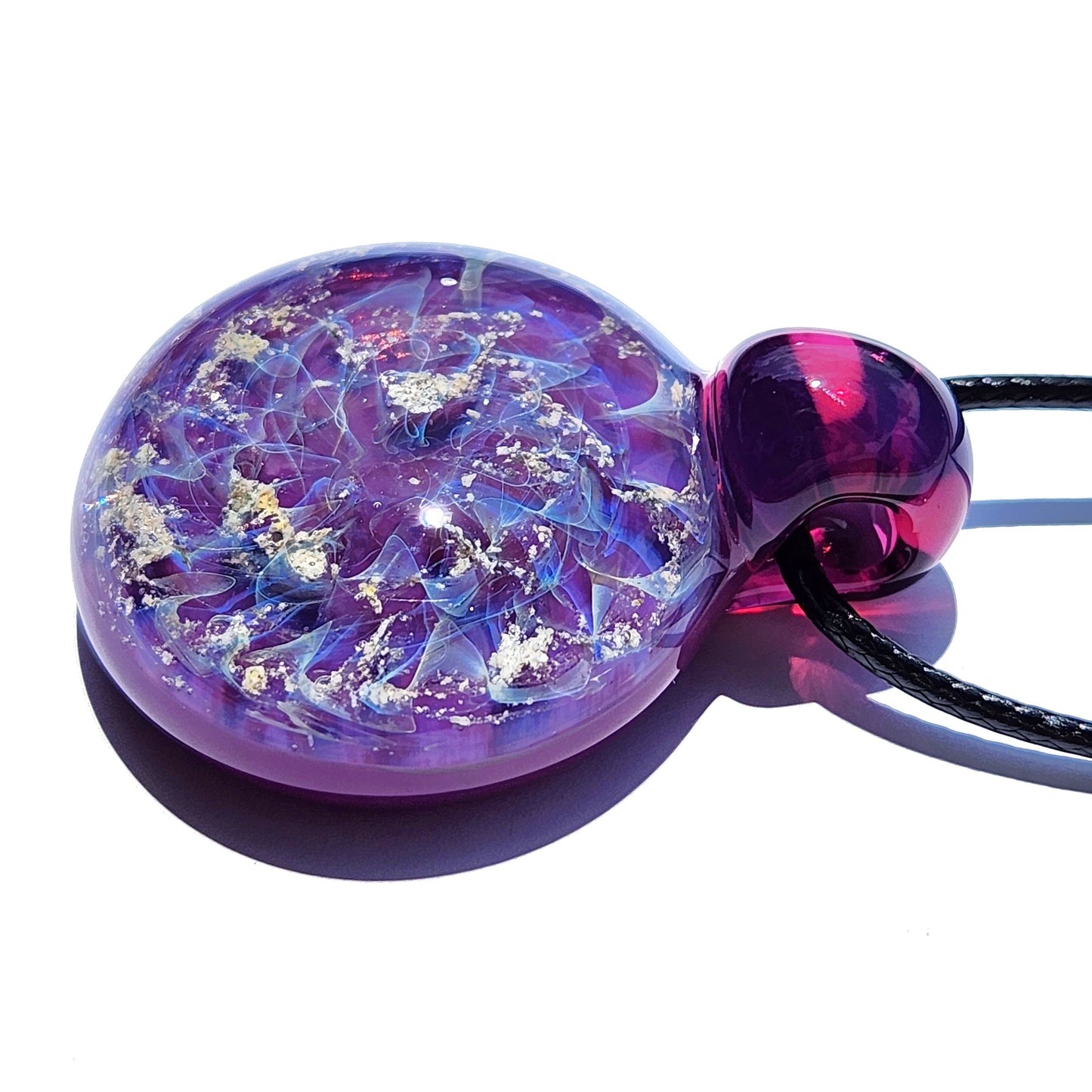 A round, purple glass ashes pendant with a dark purple top. The pendant features a swirling design of light blue and ashes flecks within the glass. The memorial pendant hangs from a black cord, creating a unique necklace.